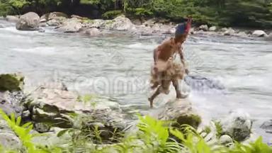 土著男子在河流边缘的岩石上跳跃